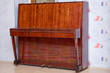 Old wooden piano. Brown piano stands against the wall . Old wooden piano keys on wooden musical instrument in front view . © Adil