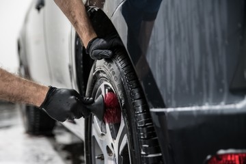 Man cleaning car wheel with brush.
