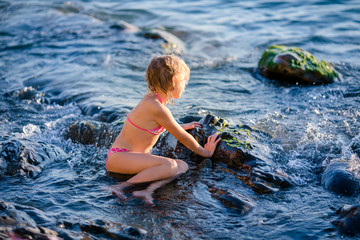 Blonde girl splashing water during summer holidays. Attractive child having fun on a tropical beach, playing with stones and water