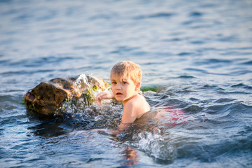 Boy splashing water during summer holidays. Attractive child having fun on a tropical beach, playing with stones and water.