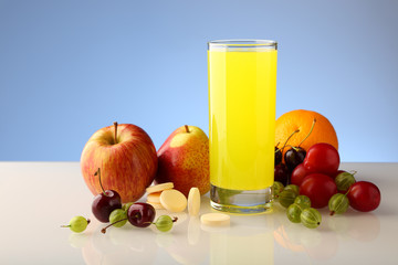 Yellow vitamin drink from effervescent soluble vitamins in tablets, in a glass beaker. Assorted fruits and vitamins in tablets.
