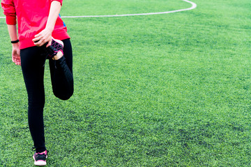 Fototapeta premium Girl in black sports leggings and a pink jacket kneads before training in an open sports arena
