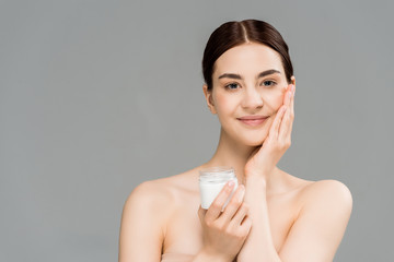 happy naked woman holding container with cosmetic cream and touching face isolated on grey