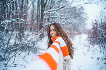 Fototapeta na wymiar Winter portrait of young woman in the winter snowy scenery. Portrait of a young woman in snow trying to warm herself.