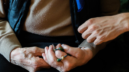 young man hand holding elderly woman hand with rosary beads. family care, praying concept.
