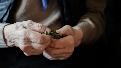 old hands of elderly woman, fingers, nails with veins. skin of aged person. aging process. rosary beads for praying. risk group coronavirus or covid virus