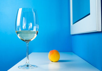a glass of white wine on a blue background is standing on a white table with a peach