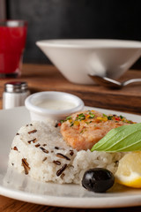 Steamed piece of salmon with boiled basmati rice in a white dish, served on a rustic wooden table