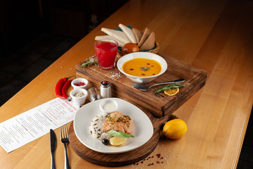 Side view of a two course meal, served on a wooden table: steamed salmon and rice, spicy pumpkin soup, fruit drink