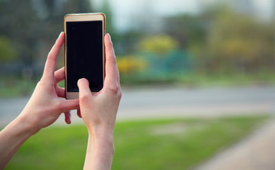 Close up of a female hand with a smartphone on the background of the city. Photograph by phone, mobile technology, black screen, place for text.