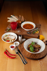 Side view of three traditional meals, served on a wooden table: red russian hot borscht, thai buckwheat noodles with vegetables and sesame, mediterranean Caesar salad with croutons and chicken