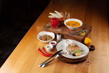 Side view of a three course meal, served on a wooden table: steamed salmon and rice, spicy pumpkin soup, thai noodles with vegetables, roasted chicken and sesame, flavoured with oyster sauce