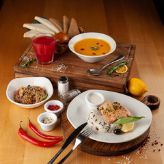 Side view of a three course meal, served on a wooden table: steamed salmon and rice, spicy pumpkin soup, thai noodles with vegetables, roasted chicken and sesame, flavoured with oyster sauce