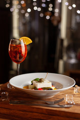 Refreshing summer cocktail Aperol Spritz and greek salad with feta cheese on black background with blurred bokeh lights