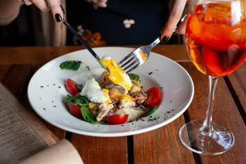 Close up cutting poached egg with liquid yolk, as a part of salad with vegetables, bacon and greens