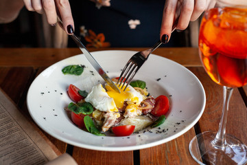 Woman is eating gourmet salad with poached egg with fork and knife on a summer terrace