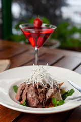 Top view of thai style marbled beef salad with sweet alcoholic strawberry cocktail on summer terrace