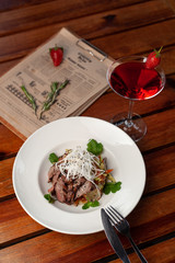 Thai style marbled beef salad with sweet alcoholic strawberry cocktail on a dark wooden table