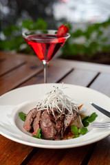 Top view of thai style marbled beef salad with sweet alcoholic strawberry cocktail on summer terrace