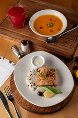Two course lunch in a restaurant, served on a wooden table: steamed salmon and rice, bright-yellow spicy pumpkin soup