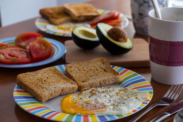 Breakfast wooden table with bread slice, fried egg, tomato and avocado