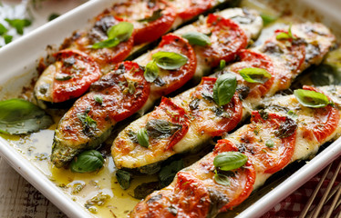 Roasted zucchini with the addition of tomatoes, mozzarella cheese, fresh basil and olive oil (caprese salad) in a ceramic baking dish, close-up. Nutritious and tasty vegetarian dish