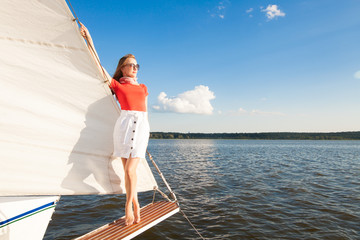 Model in a red blouse, white skirt, glasses, a red scarf on his head, standing on a white yacht, overlooking the sea and the blue sky, with a place for the inscription. The concept of luxury.