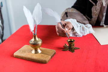 cropped view of victorian man holding feather near ink and paper