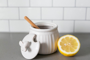 White Ceramic Honey Pot with Wooden Honey Dipper and Lemon Slice, White Subway Tile Background in Kitchen