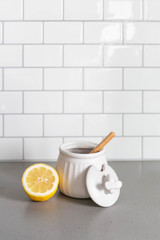 White Ceramic Honey Pot with Wooden Honey Dipper and Lemon Slice, White Subway Tile Background in Kitchen