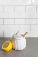 White Ceramic Honey Pot with Wooden Honey Dipper and Lemon Slice, White Subway Tile Background in Kitchen