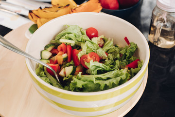 Close-up of tasty homemade salad made of delicious fresh home veggies. Tomatoes, cucumbers, salad cut in bowl with serving spoon or fork on the table.