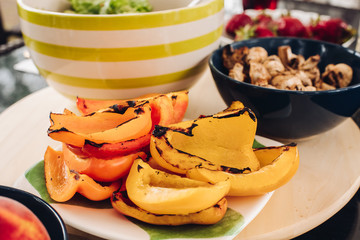 Selective focus of grilled yellow pepper standing on plate. Fresh healthy vegetables, champignons cooked on grill and vegetable salad on table. Concept of vitamins and picnic.
