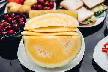 Close-up of sliced yellow watermelon served on the table with variety of healthy and organic fruit and vegetables.