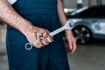 cropped view of auto mechanic with mud on hand holding hand wrench in car repair station