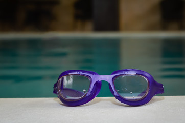 Close-up of  blue swim goggles at the  edge of  an interior swimming pool .