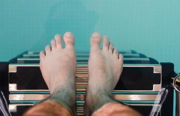 Man with bare feet descending on the ladder in the pool .