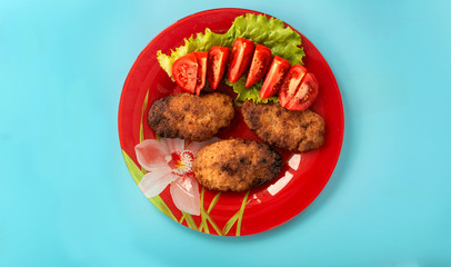 Meatballs with salad and tomatoes in a plate on a turquoise background, top view
