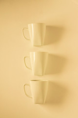 3 yellow coffee mugs on yellowish background in a vertical row, empty copy space