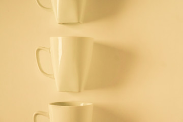 Yellow coffee mugs on yellow background in a vertical row with empty copy space