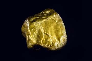 Gold nugget, large gold stone closeup isolated on black background. Concept of finance, luxury or wealth.
