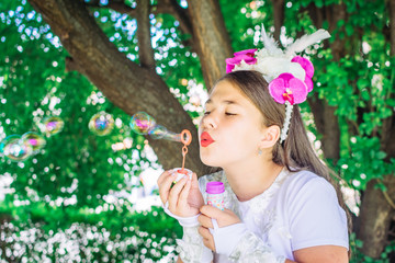 Cute, little girl with flowery hair decorative accessory blowing soap bubbles.