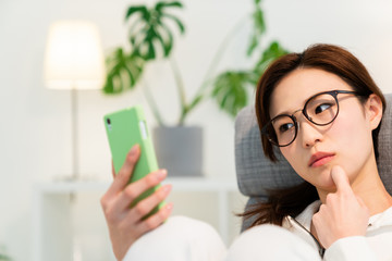 部屋でスマホを見る女性　考える