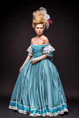 beautiful victorian woman in wig standing in blue dress on black