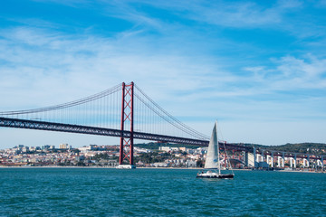 The 25th of April brige over the River Tagus with a sailboat in Lisbon, Portugal