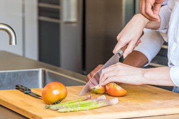 Female hand cut tomatoes on rustic kitchen table, cooking and vegetarian concept.