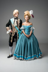attractive victorian woman in blue dress near handsome man with hand on hip on grey