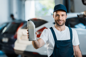 happy car mechanic in cap holding bottle with car oil