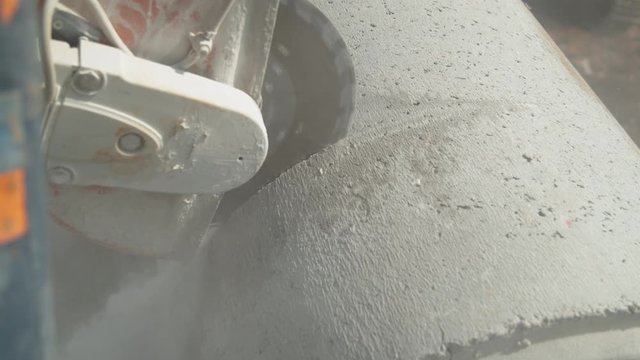 CLOSE UP: Angular saw grinding through a concrete tube at a construction site. Sharp circular cutter blade spins before grinding into a gray concrete tube. Builder cutting into a large concrete pipe