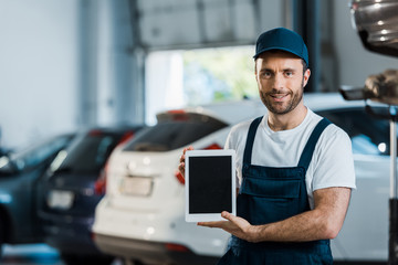 cheerful car mechanic holding digital tablet with blank screen in car service